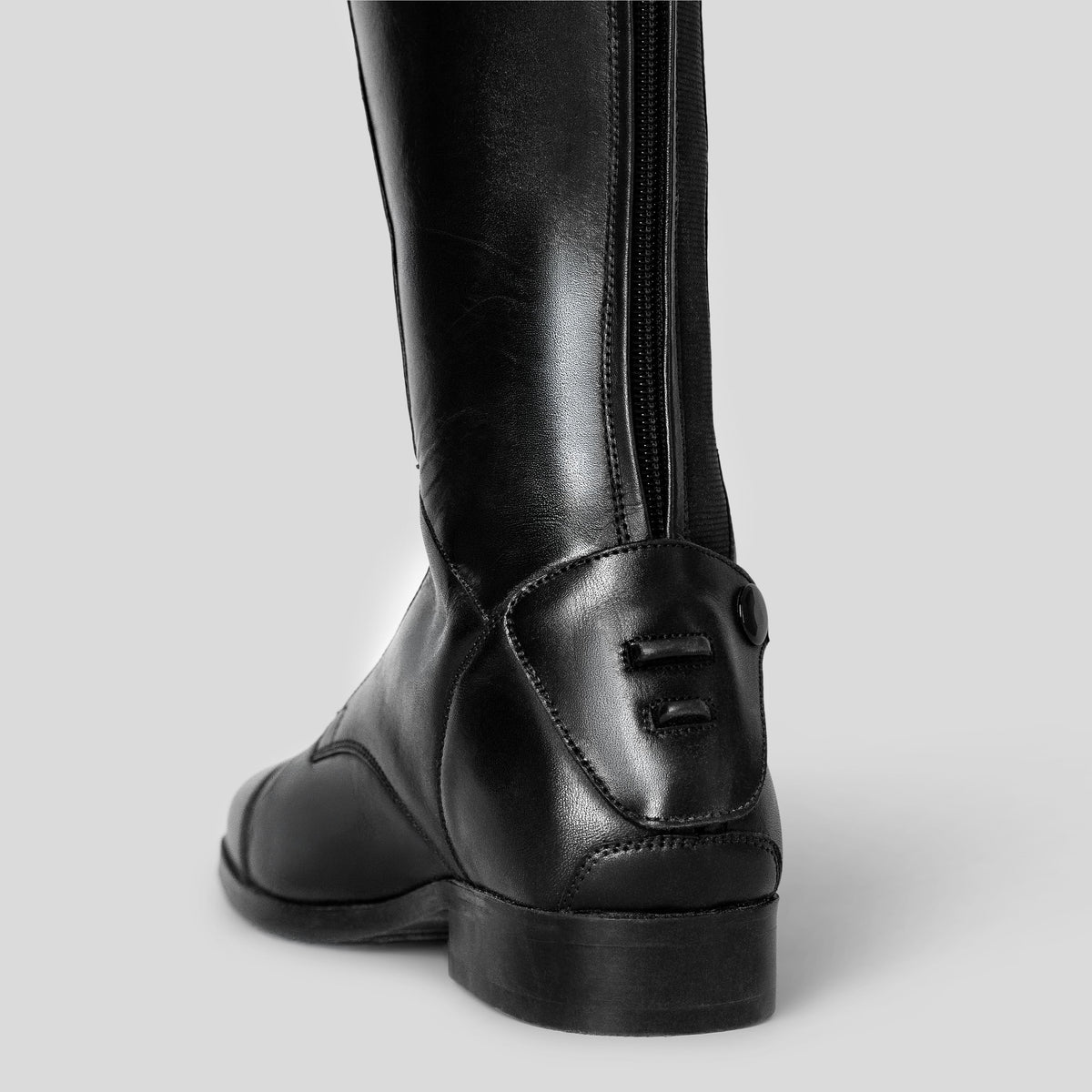 A close-up rear view of a black leather riding boot with a back zipper 